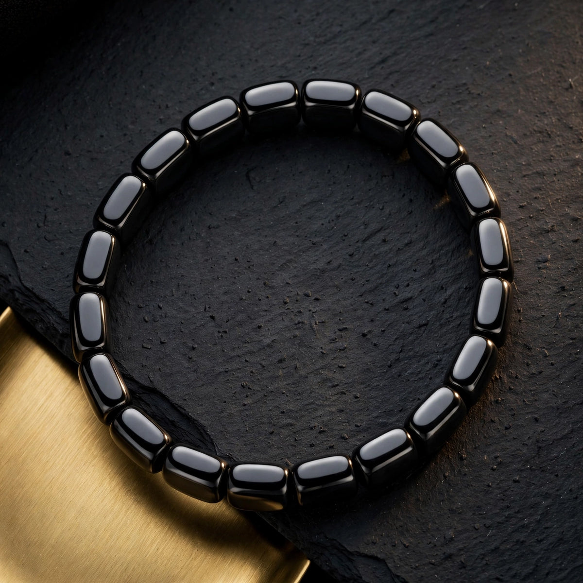 Black hematite tile bracelet on dark slate with a brushed gold tray